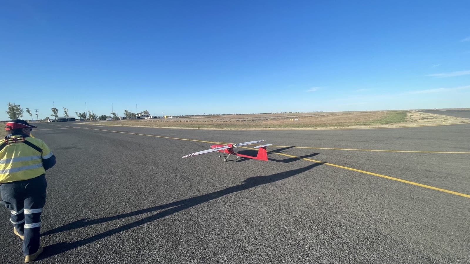 Pilot in high-visibility gear preparing a fixed-wing survey drone on an airstrip