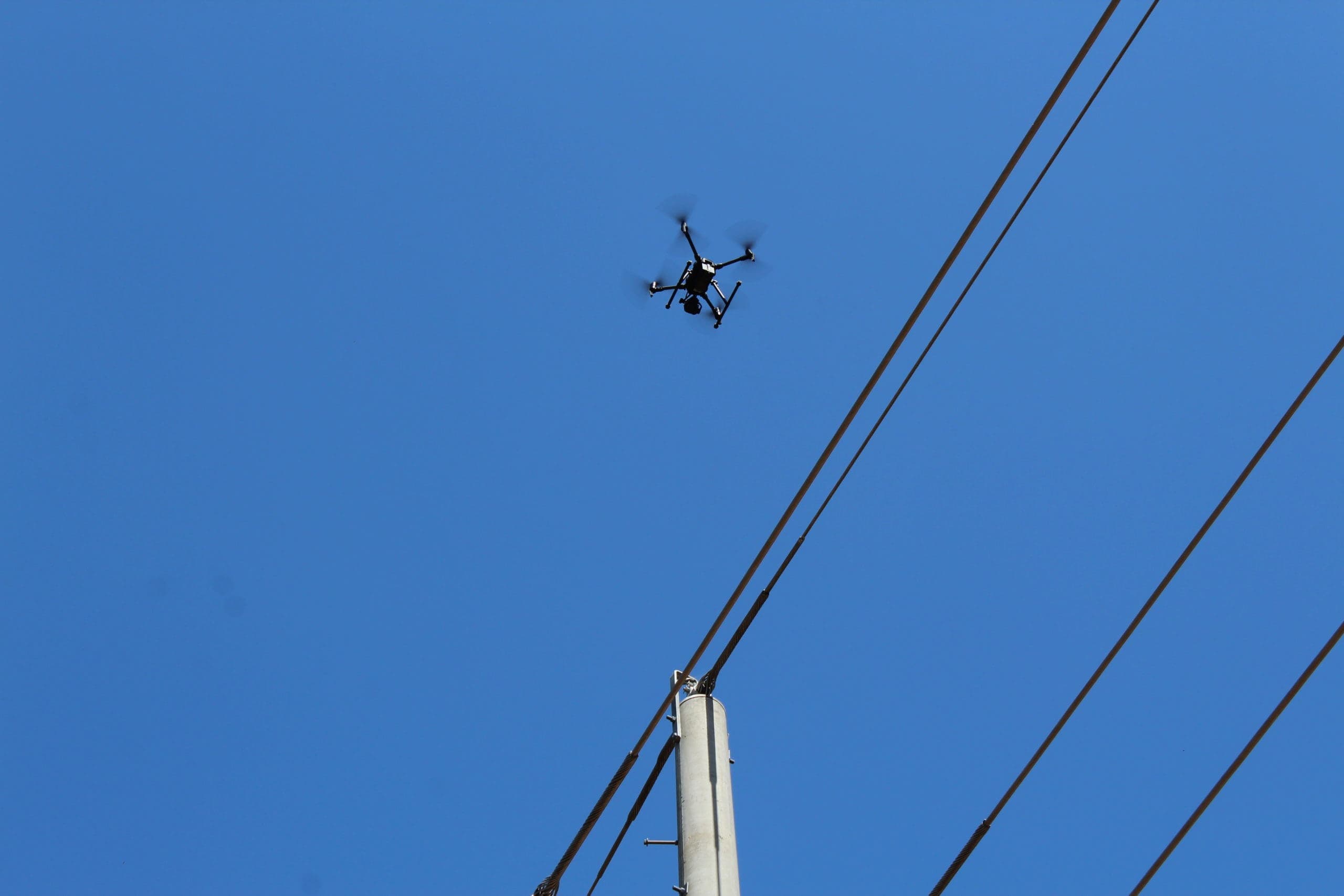 Drone inspecting a powerline against a clear blue sky